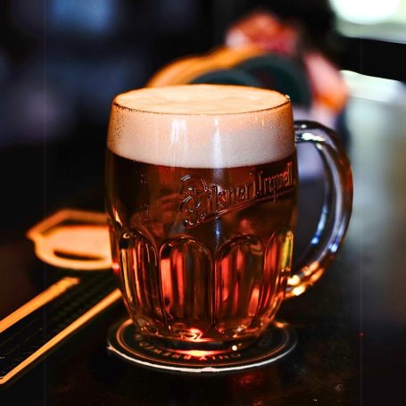 Ein Pilsener Urquell Bierkrug mit schaumiger Oberfläche auf einem Untersetzer in einer Bar.