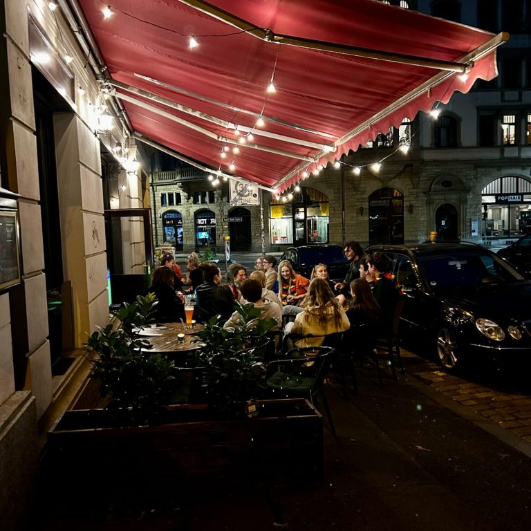 Eingedeckte Tische unter Lichterketten im Außenbereich der Bar Tollkühn bei Nacht.