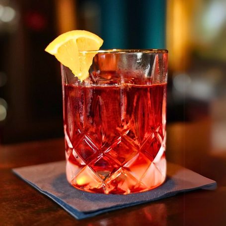 Negroni Cocktail mit einem Stück Orange in einem Kristallglas auf einem Untersetzer.